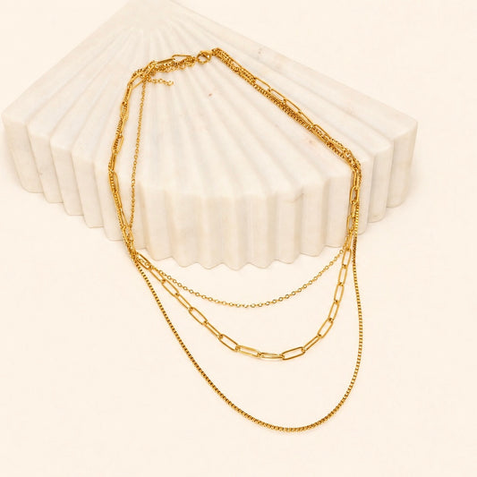 Gold layered chain necklace on a textured white surface