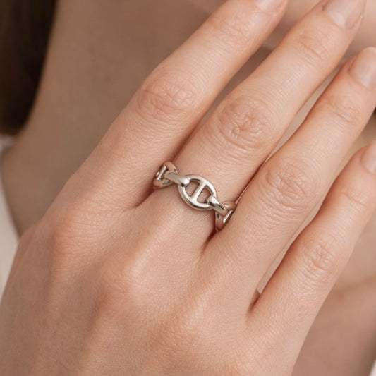 Silver ring with a unique design on a person's finger against a neutral background