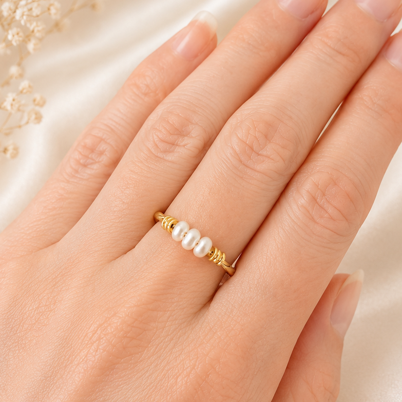 Hand wearing a gold ring with pearls on a soft fabric background