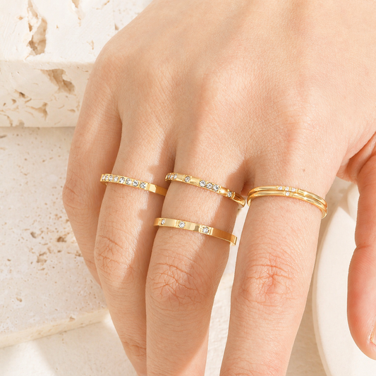 Gold rings with small diamonds on a hand against a neutral background