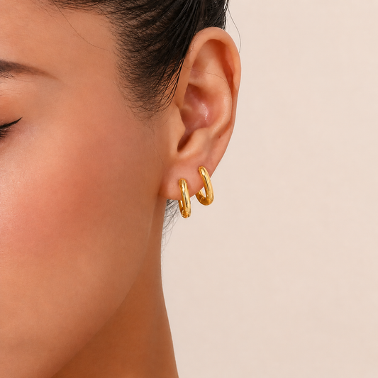 Close-up of a person wearing gold hoop earrings on a beige background