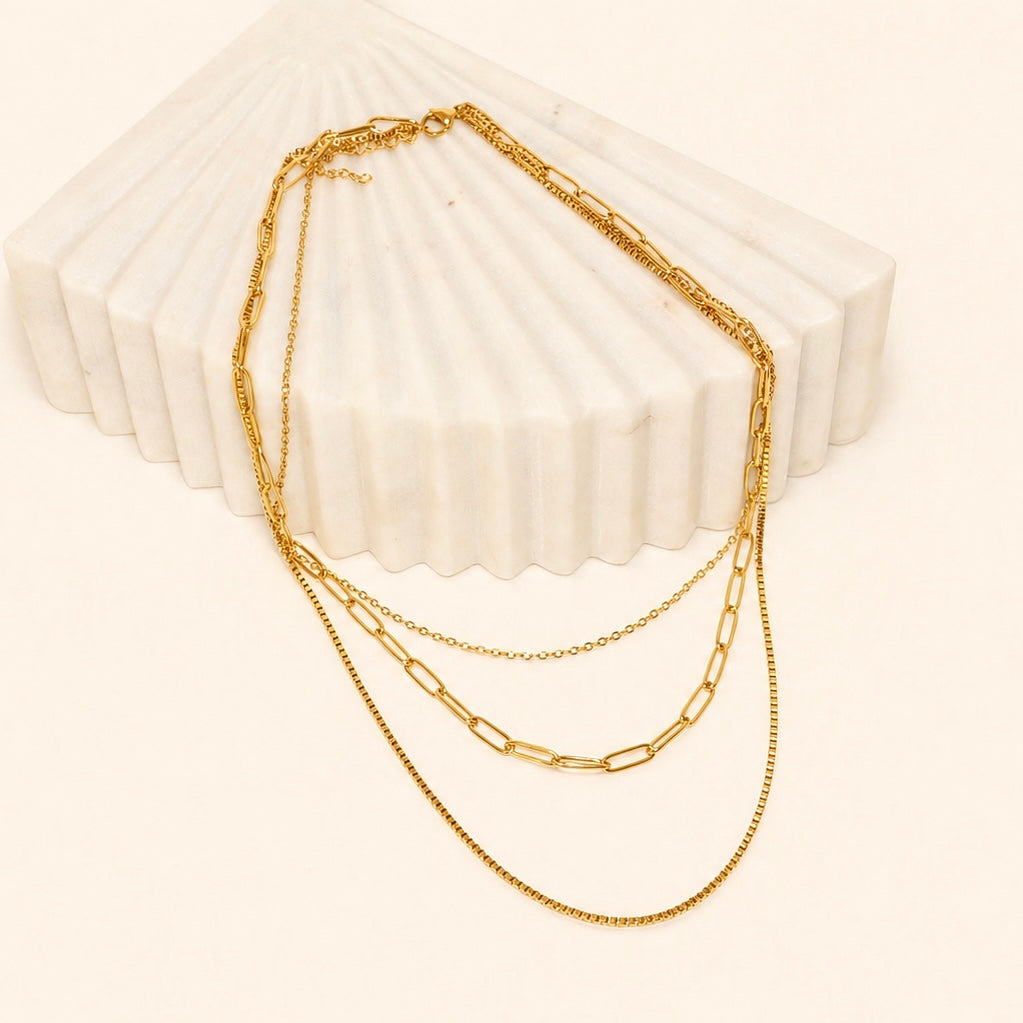Gold layered chain necklace on a textured white surface