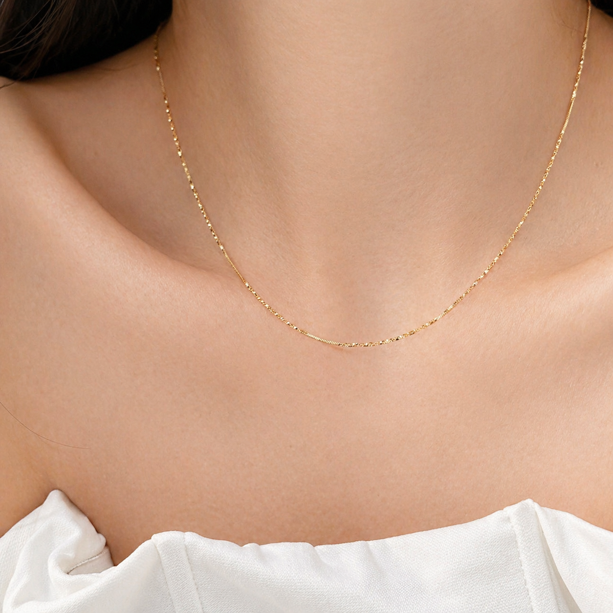 Gold necklace on a person wearing a white top