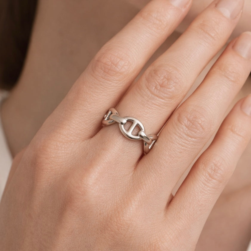 Silver ring with a unique design on a person's finger against a neutral background